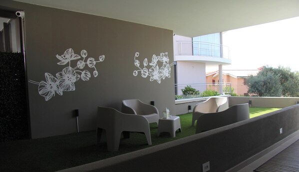 A balcony with modern chairs and a small table, a wall with floral decals, and a view of a building with a balcony. - SandBeach Apartment - Modern apartment 700 meters from paradise beach (Golfo Aranci)