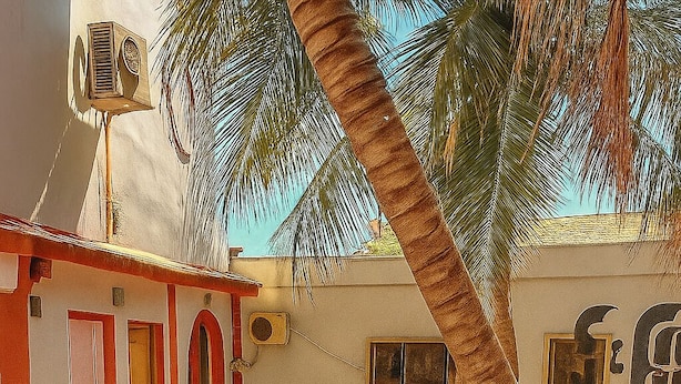 Ein gebogener Balkon mit Sitzgelegenheit, Palmen und einem Gebäude mit Wandgemälde.