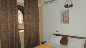 Ein Schlafzimmer mit Bett, Vorhängen, einer Klimaanlage, einer Wandleuchte und einem floralen Gemälde.