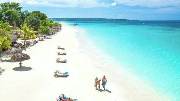 Una spiaggia con sabbia bianca, acqua cristallina turchese e alcune persone che passeggiano.