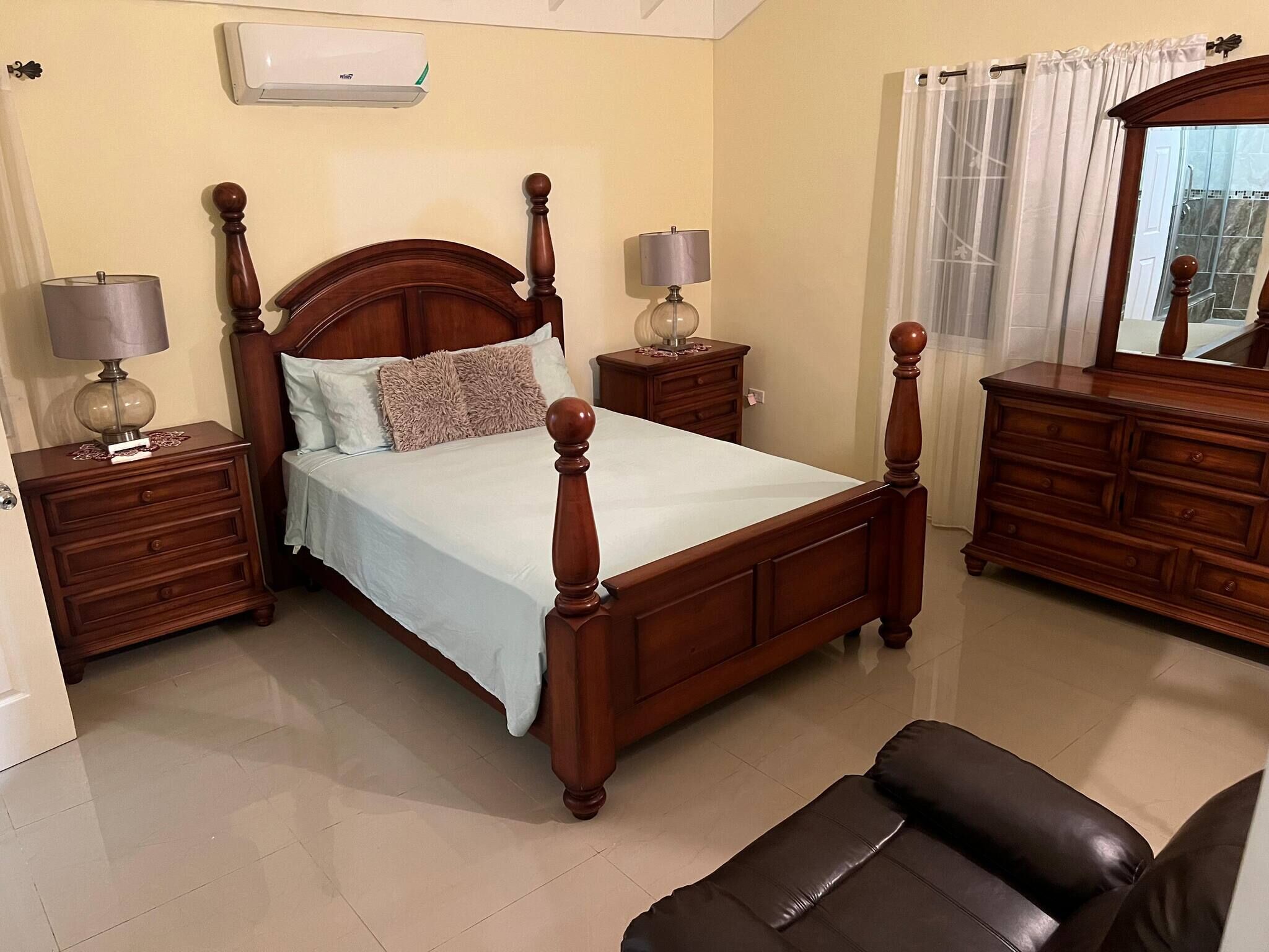 Une chambre à coucher avec un lit à baldaquin en bois, deux tables de chevet avec des lampes, une commode et un miroir.