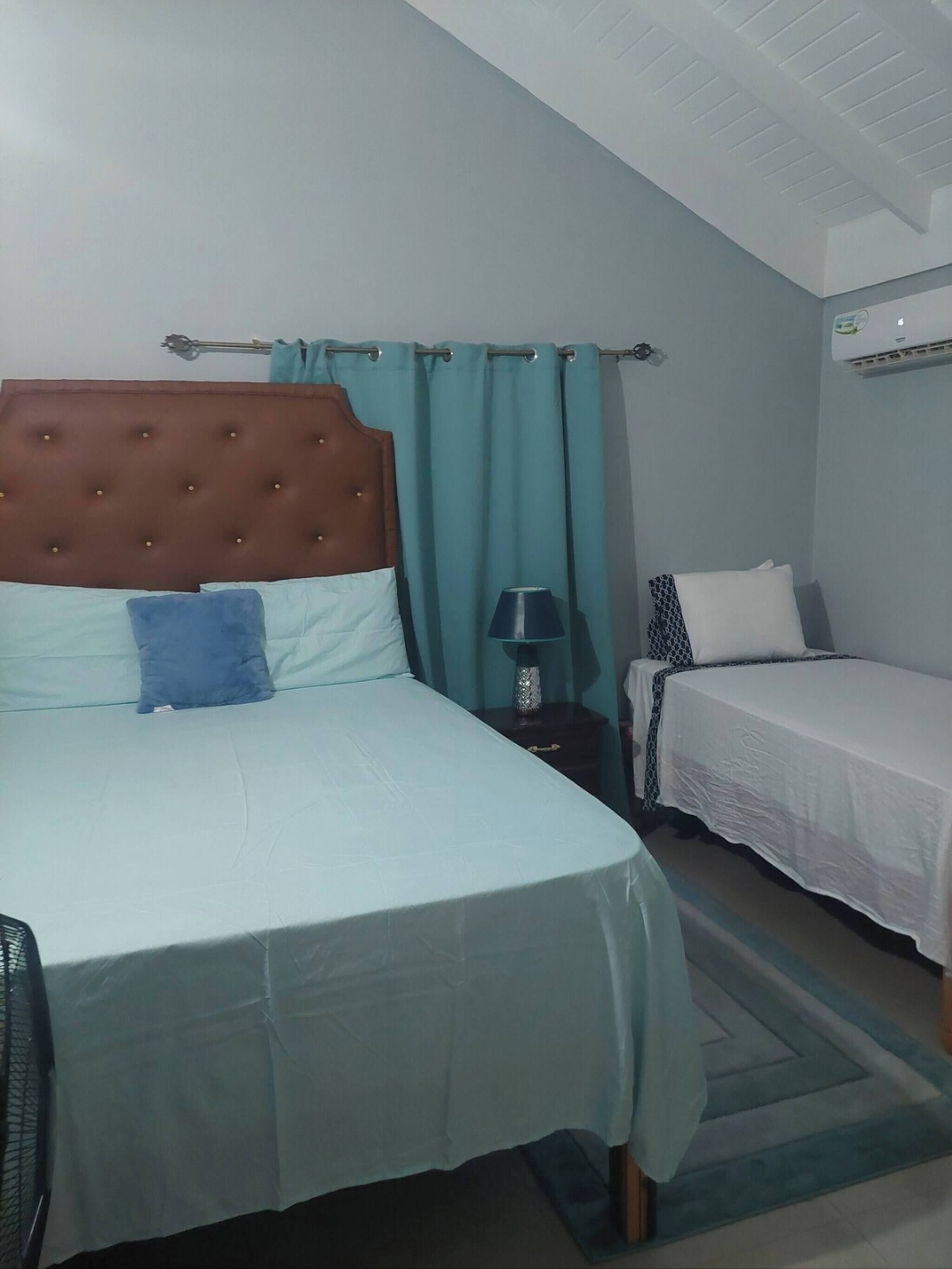 Ein Hotelzimmer mit einem Einzelbett, einem kleineren Bett, einem Nachttisch mit Lampe und einer Klimaanlage an der Wand.