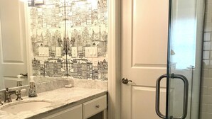 Un baño con papel tapiz de paisaje urbano, un lavabo, un espejo, una cabina de ducha de cristal y suelo de baldosas.