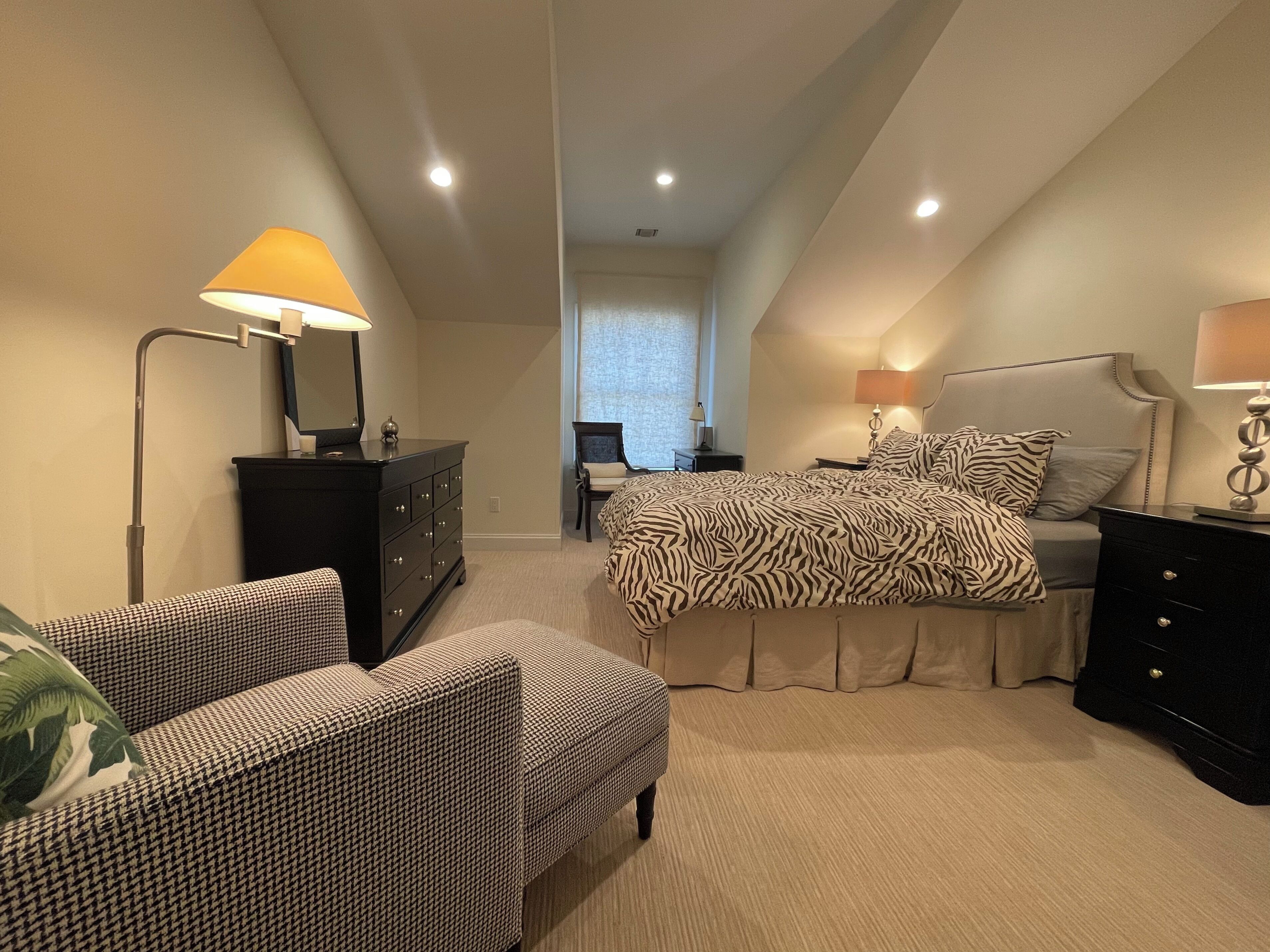 Un dormitorio con cama, una silla, un aparador y un escritorio con lámpara.