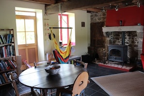 A dining area with a round table, chairs, a bookshelf, a hammock, and a fireplace.