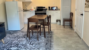 Una cocina compacta con armarios blancos, un refrigerador, un microondas y una mesa de comedor con sillas.