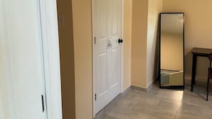 Un pasillo con una puerta blanca, paredes color beige, un espejo y una mesita.