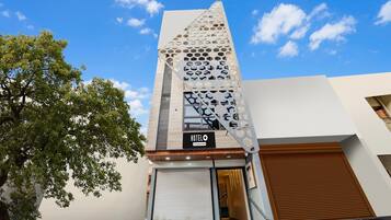 Un hotel con diseño moderno, que destaca por su fachada geométrica, una escalera que conduce a la entrada y una puerta de acceso visible.