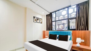 Ein Hotelzimmer mit Bett, Nachttisch, Lampe, einem Fenster mit Vorhängen und Wandbildern.