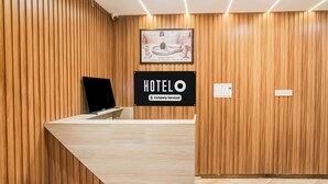 Ein Hotelrezeptionstresen mit einer Wandpaneelaus Holz, einem gerahmten Bild darüber und einem Schild mit der Aufschrift 'HOTEL Company-Serviced'.