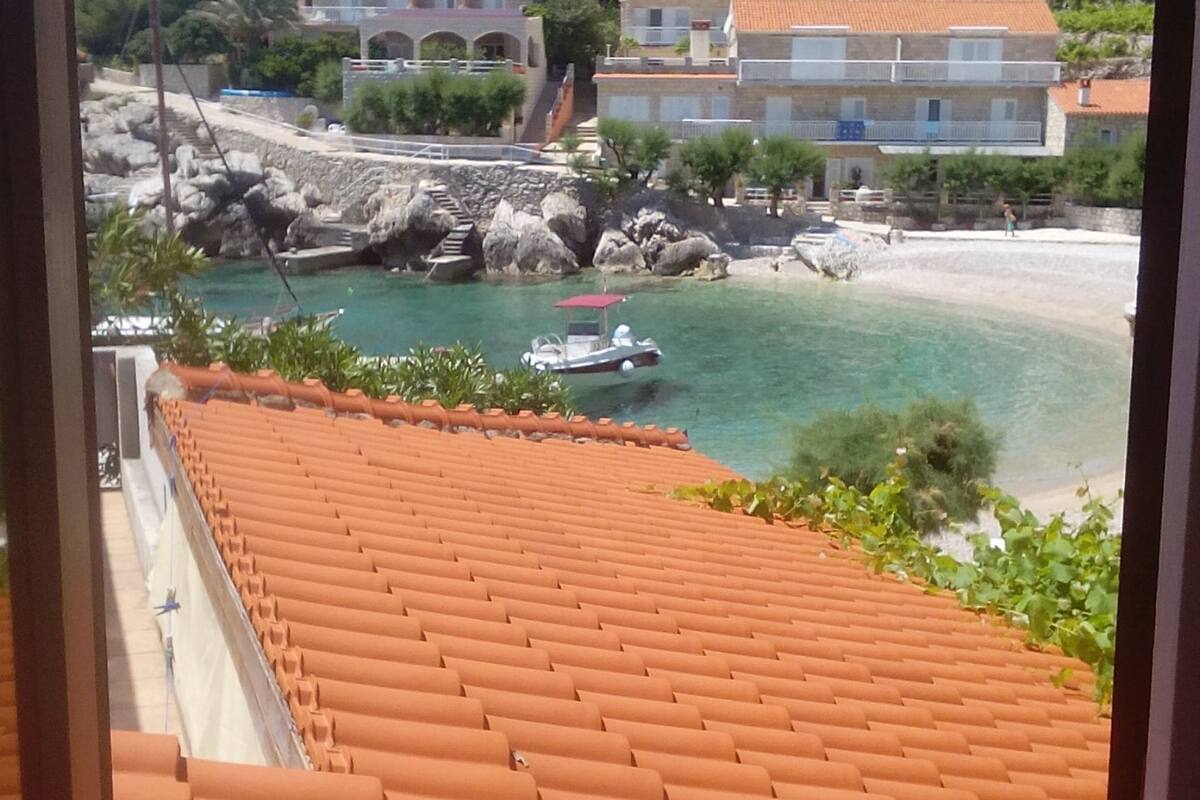 A coastal view with a tiled roof, rocky shoreline, and a boat in the water.