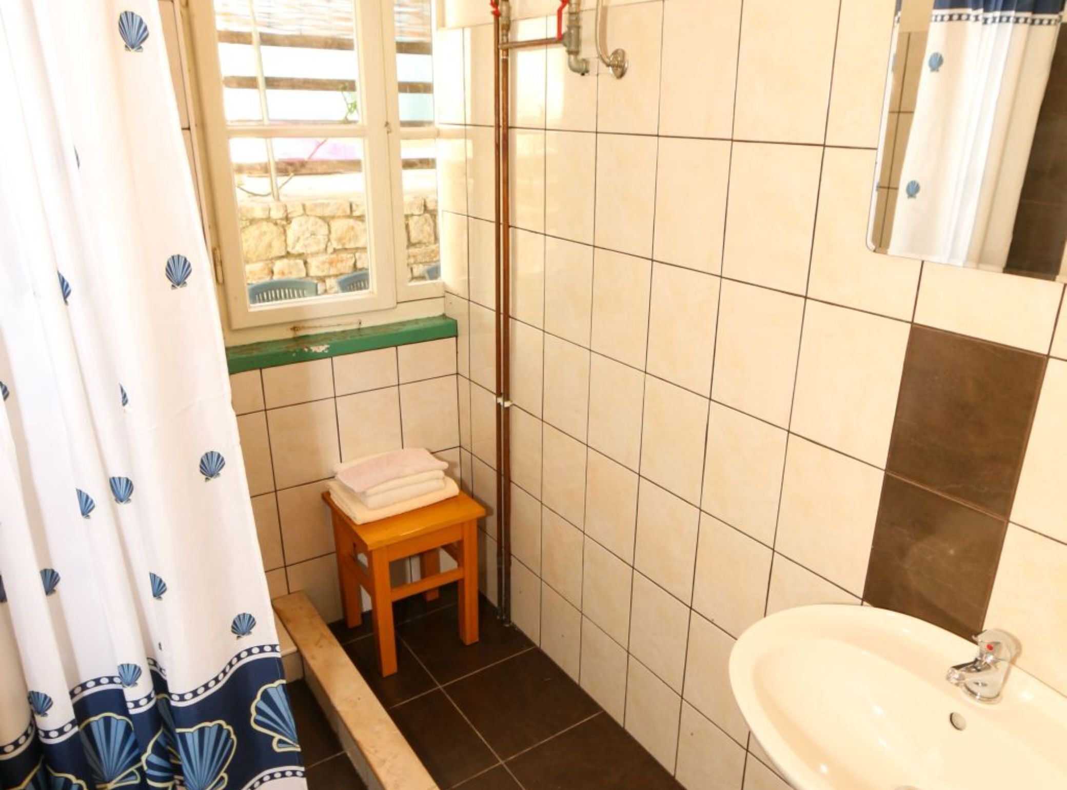 A bathroom with a sink, a mirror, a shower, and a window with a view of the outside.