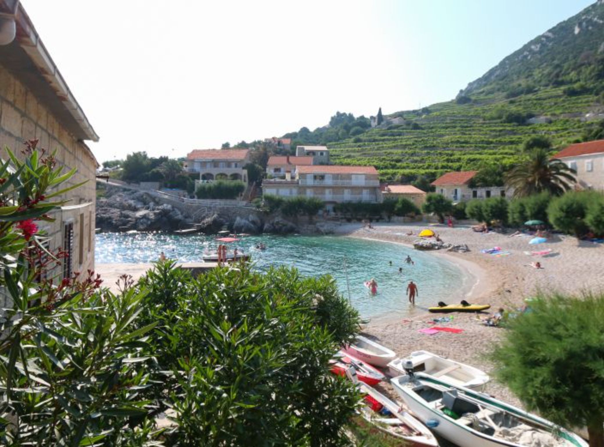 A coastal beach with boats, a rocky shoreline, and buildings in the background.