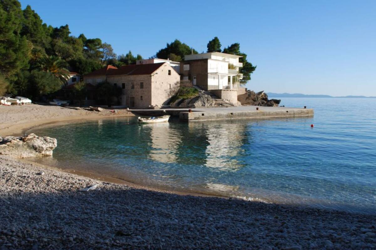 A coastal building with a stone facade, a small bridge, and a pebble beach.