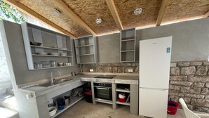 A compact kitchen with a stone wall, built-in shelves, a sink, a stove, and a refrigerator. - Apartments Trojanović (Orebic)