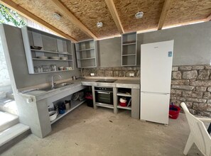 Une cuisine compacte avec un mur en pierre, des étagères intégrées, un évier, une cuisinière et un réfrigérateur.
