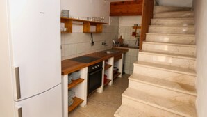 A kitchen with a white refrigerator, wooden shelves, a stove, and a marble staircase. - Apartments Trojanović (Orebic)