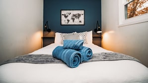 Una cama hecha con pulcritud, toallas enrolladas, un mapa del mundo en la pared y dos lámparas de pared.