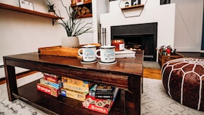 Una sala de estar acogedora con una mesa de centro de madera, estanterías, una chimenea y juegos de mesa.