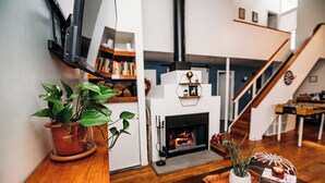 Una sala de estar moderna con chimenea, piso de madera, una escalera y un televisor montado en la pared.