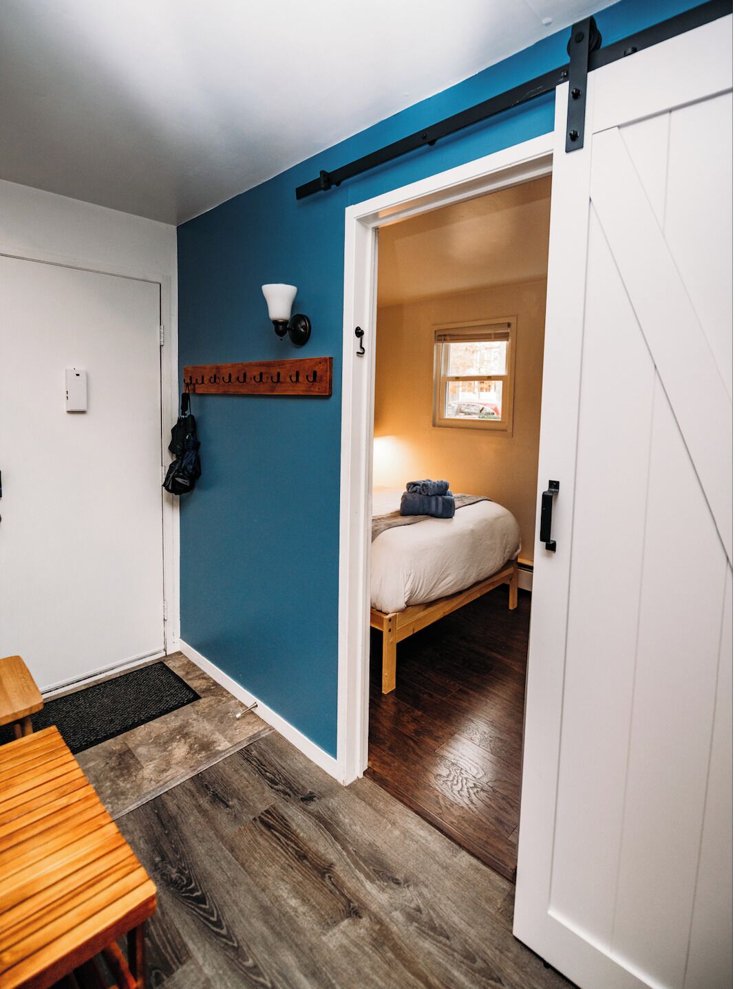 A room with a bed, a small window, a coat rack, and a door leading to another room.