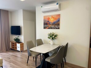 A modern room with a dining table, chairs, a TV, a painting, and a plant.
