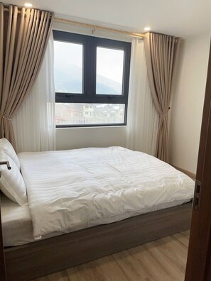 Un dormitorio con cama, cortinas, una ventana y vistas a edificios.
