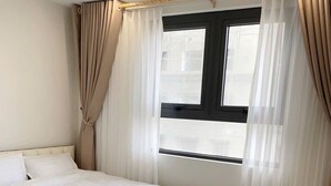 Un dormitorio con cama, cortinas, ventana y radiador.