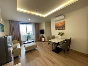 A modern living room with a dining area, a flat-screen TV, and a balcony with curtains.