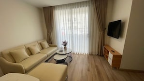 A modern living room with a sofa, ottoman, coffee table, and a flat-screen TV mounted on the wall.