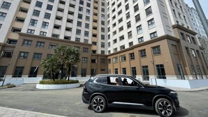Un edificio de varios pisos con diseño moderno, que incluye un área de estacionamiento con un SUV negro.