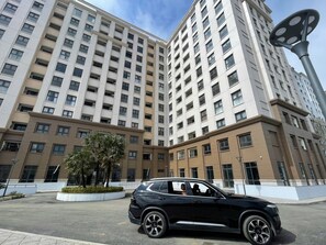 A multi-story building with a modern design, featuring a parking area with a black SUV.