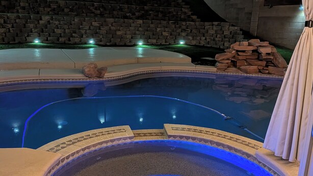 Une piscine avec un jacuzzi, des murs en pierre et un éclairage d’ambiance.