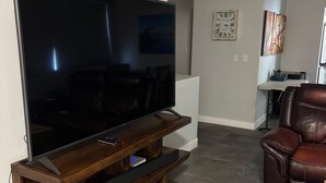 Un salon avec un grand téléviseur à écran plat posé sur un meuble en bois, un canapé en cuir et, au fond, un coin repas.