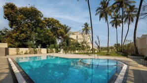 Una piscina de borde curvo, rodeada de palmeras y un edificio al fondo.