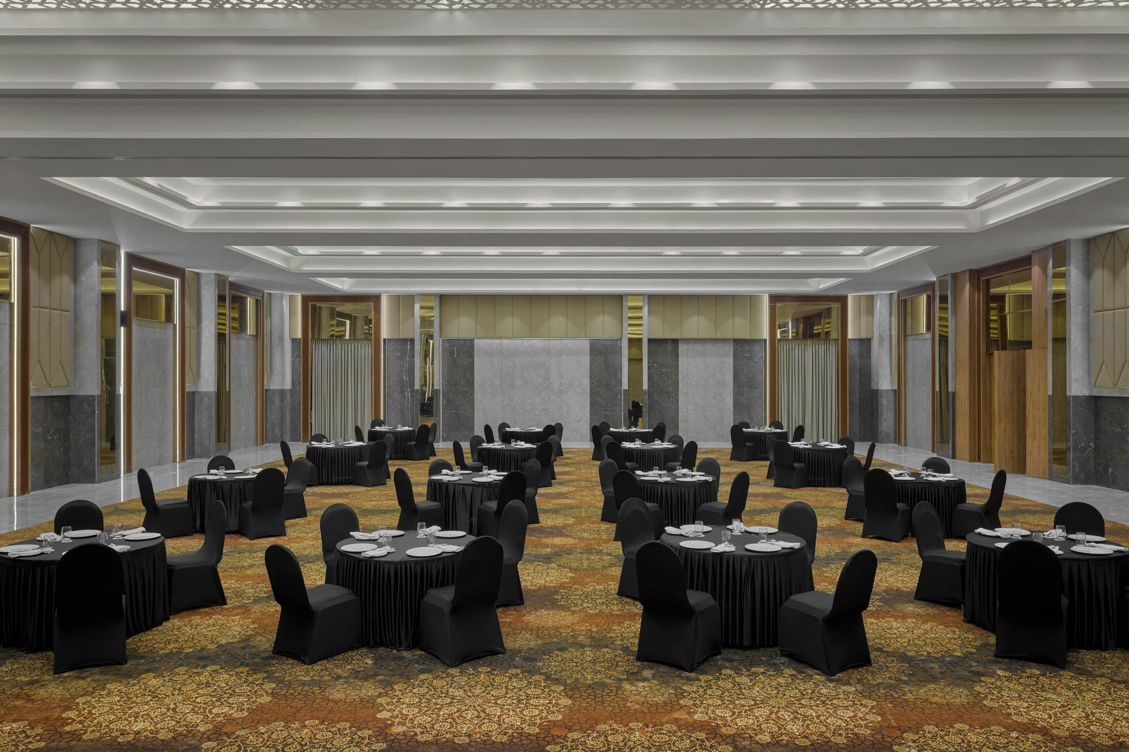 A conference room with multiple round tables and chairs, a patterned carpet, and a modern ceiling design.
