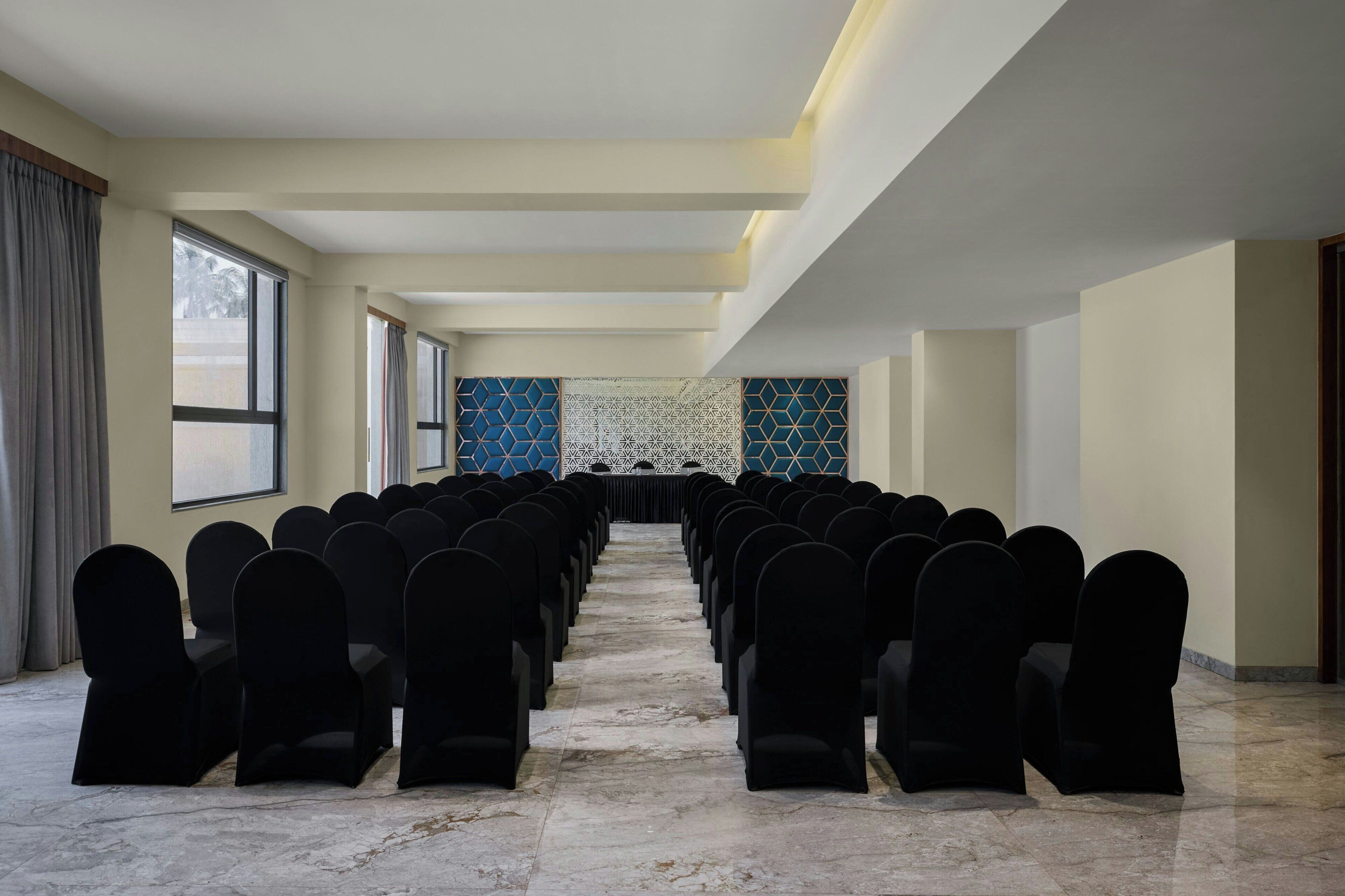 A conference room with rows of chairs, a patterned wall, and large windows.