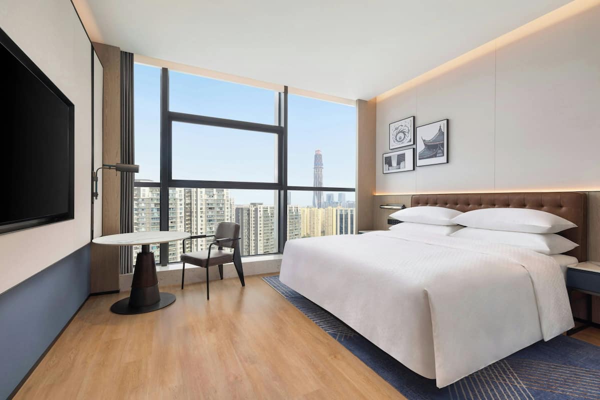 Una habitación de hotel con un ventanal grande, una cama, un escritorio y una silla.