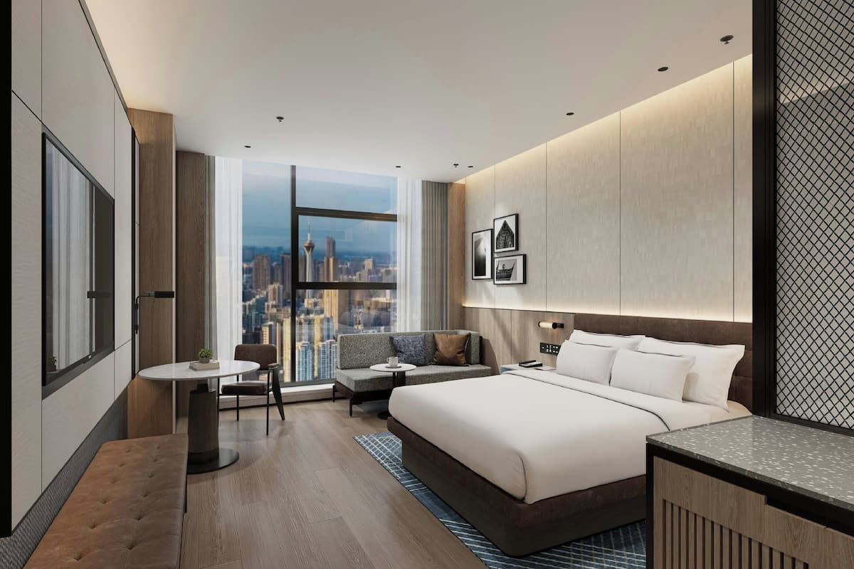 Habitación de hotel moderna con una cama grande, un área de descanso, una mesita y vistas a la ciudad.