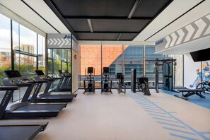 Un gimnasio con cintas de correr, máquinas de pesas y un ventanal con vistas a la ciudad.
