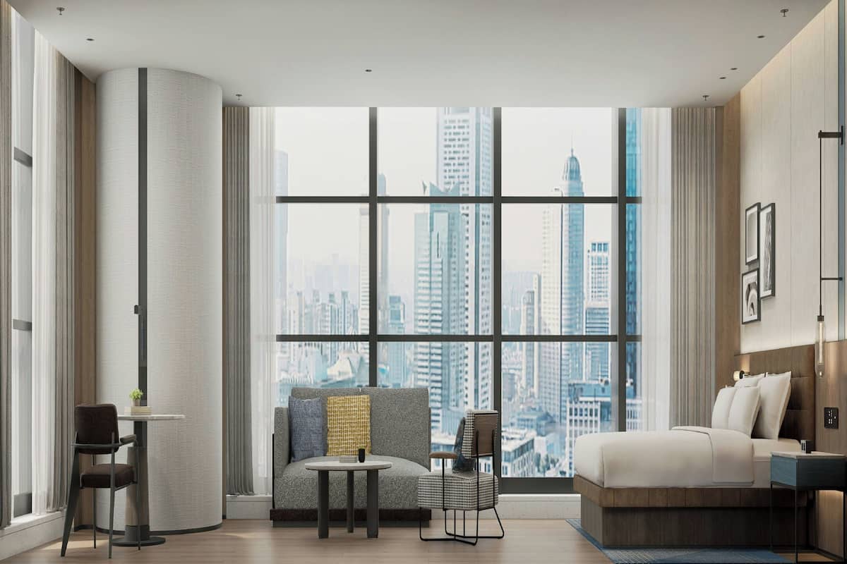 Una habitación de hotel moderna con un ventanal grande, un sofá, una cama y una pequeña mesa.
