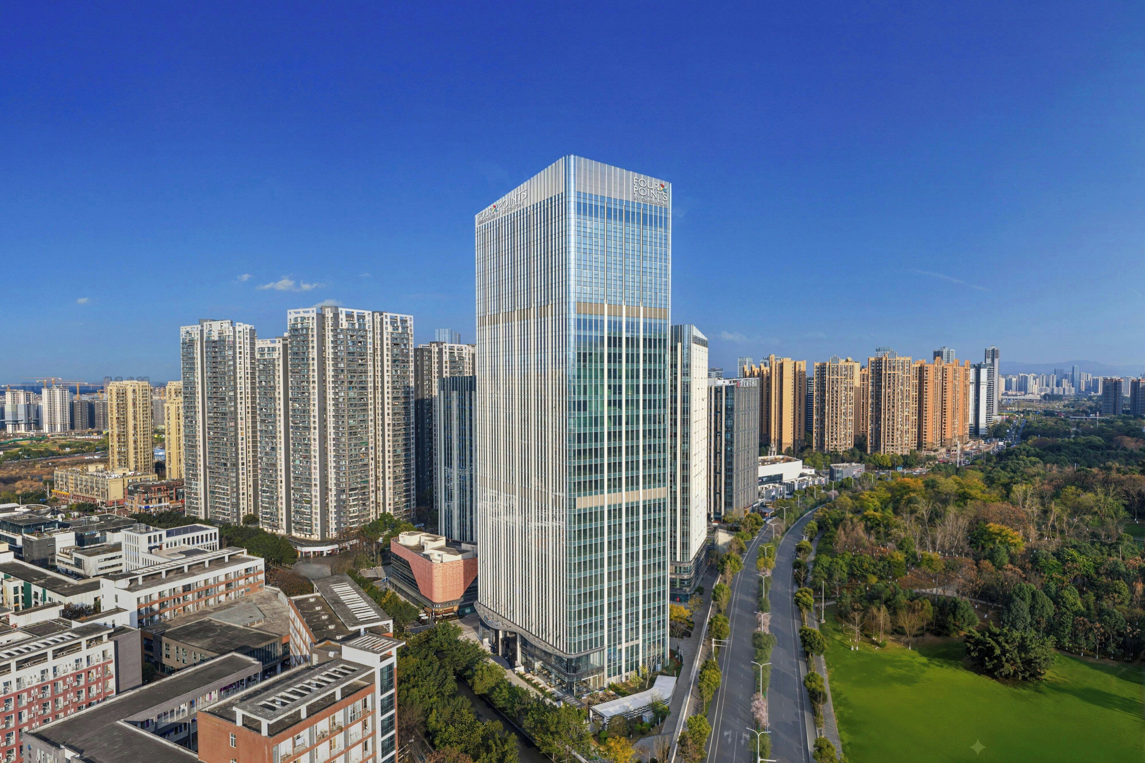 A high-rise building with a glass facade, surrounded by other tall buildings and a park.