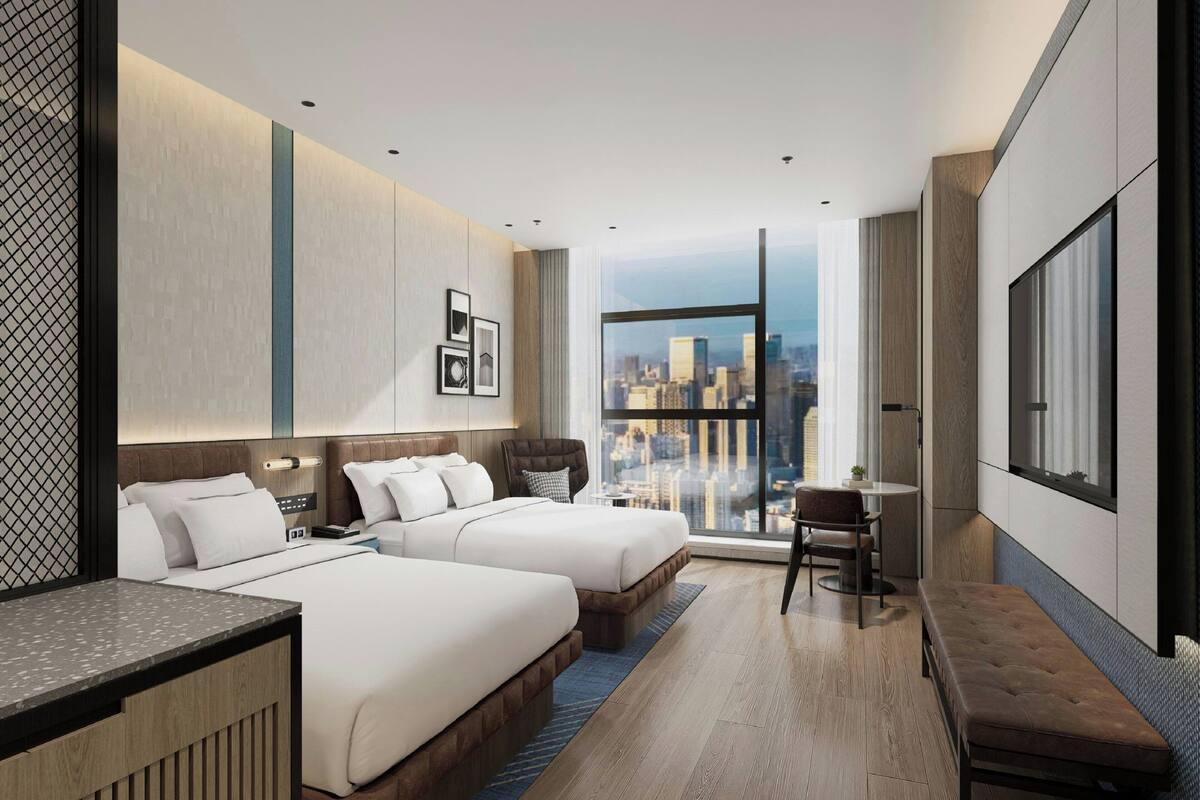 Habitación de hotel moderna con dos camas, un escritorio, una silla y un amplio ventanal con vistas a la ciudad.