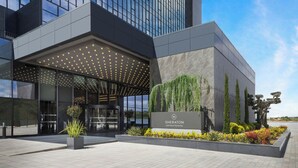 A modern hotel entrance with a covered area, a signboard, and landscaped garden.