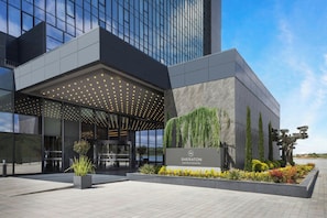 A modern hotel entrance with a covered area, a signboard, and landscaped garden.