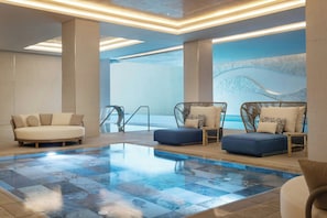 Un área de piscina interior moderna con sillones de descanso, suelo estampado y vista al mar.