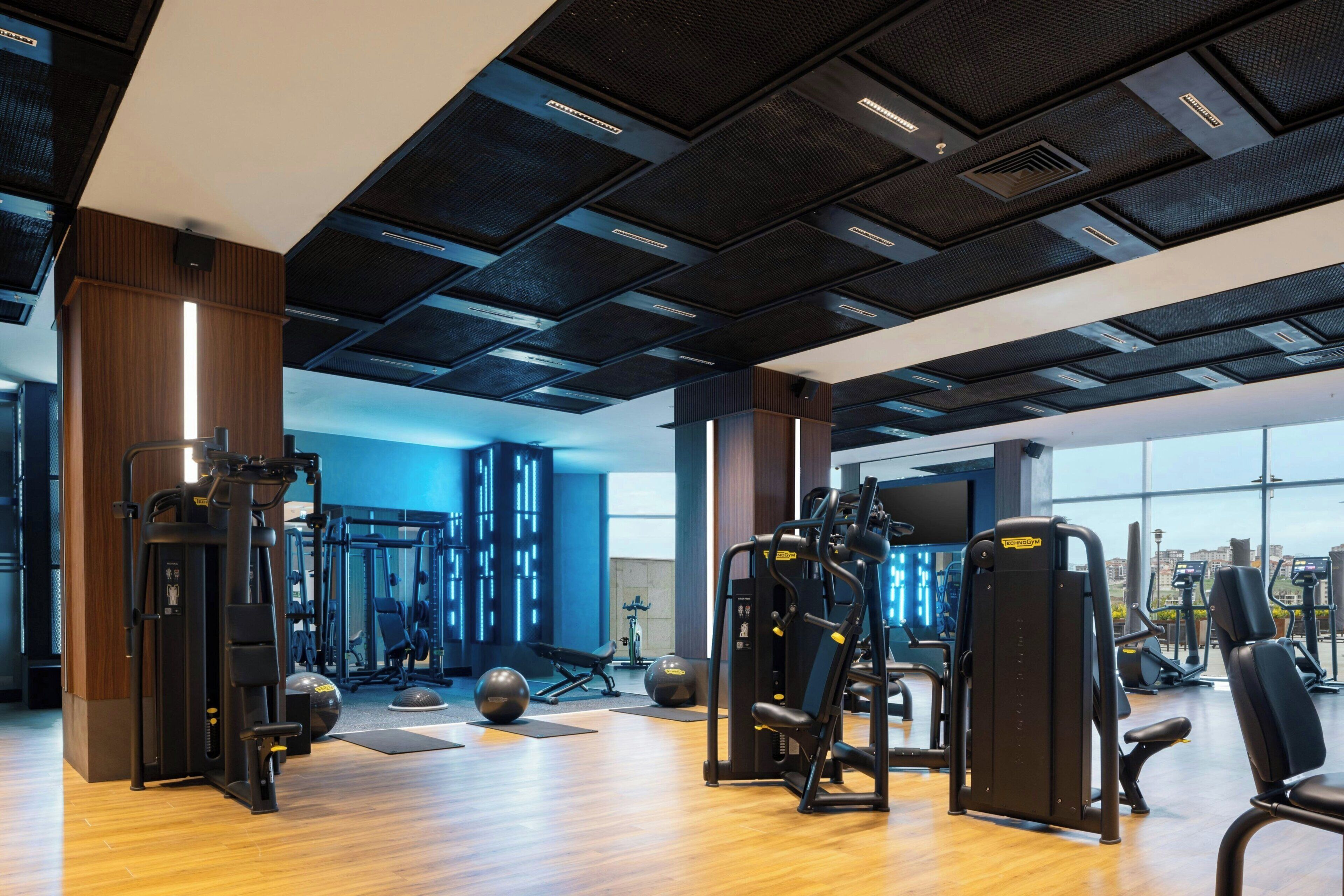 A gym with various exercise equipment, wooden flooring, and large windows offering a view.