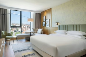 A hotel room with a large bed, a desk, a chair, a view of the city, and a patterned wall.