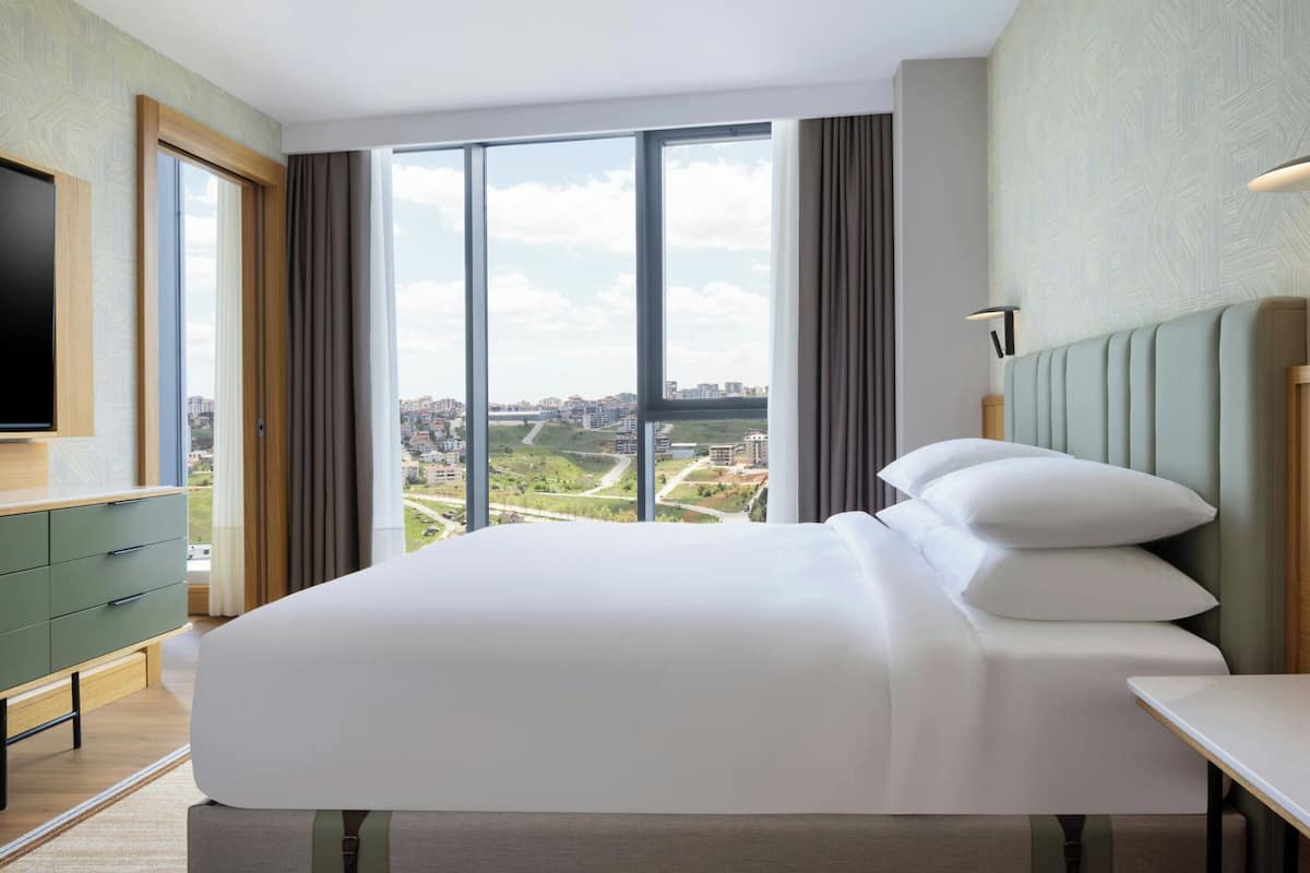 Une chambre d’hôtel avec un grand lit, une télévision, un bureau et une vue sur le paysage urbain, grâce à de grandes fenêtres.