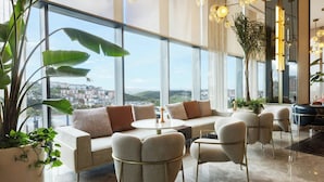 A modern interior with a sofa set, chairs, a round table, and large windows offering a city view.